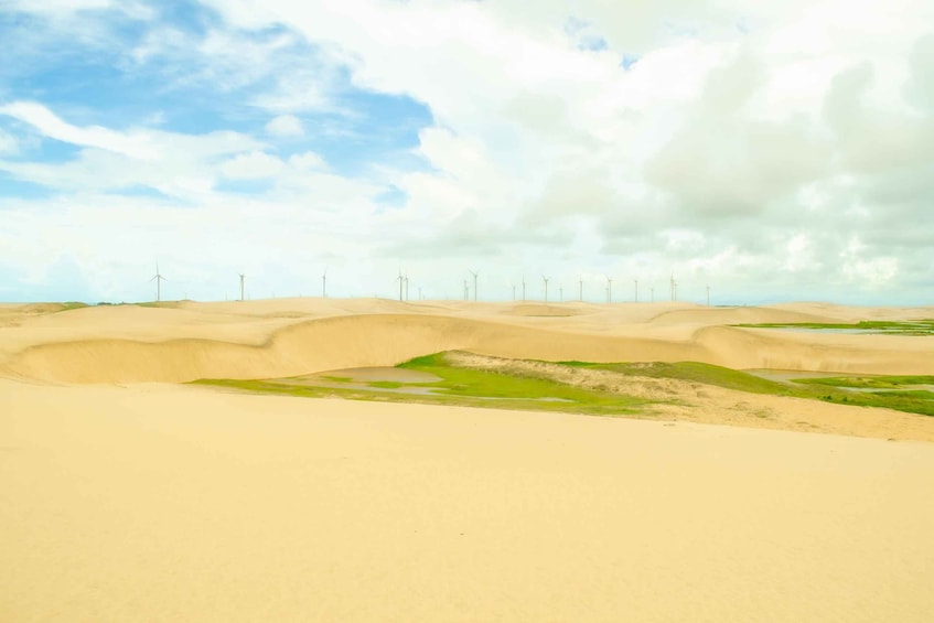 A desert landscape with sand dunes and wind turbines in the distance. 1