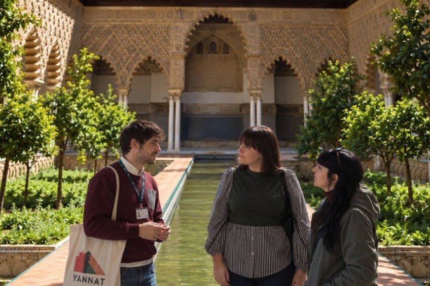 Three people standing in a courtyard with ornate arches and a water channel. 1