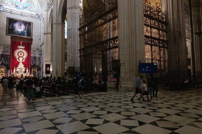 A large cathedral interior with a checkered floor, a large altar, and a crowd of people. 2