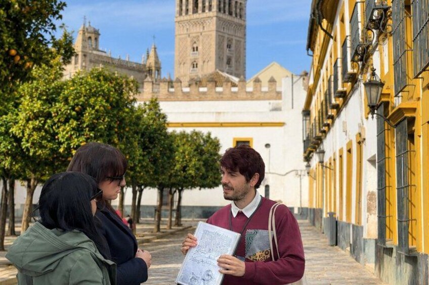 A person holding a map, standing on a cobblestone street with buildings and a tower in the background. 1