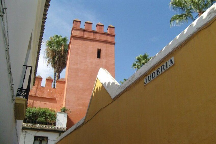 A building with a tower, a palm tree, and a sign that reads 'JUDERIA'. 4