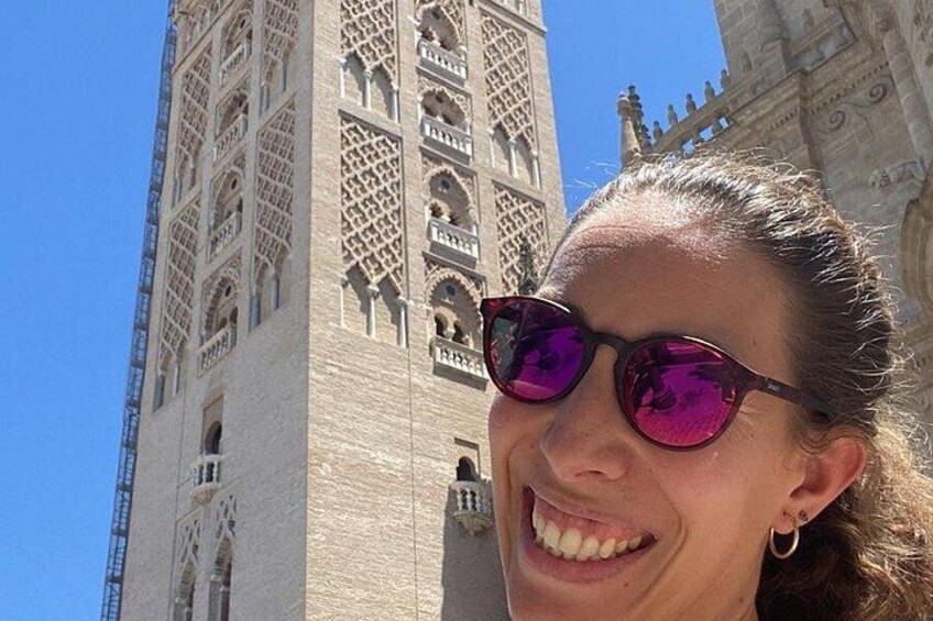 A person in front of a tall, intricately designed tower with a clear blue sky in the background. 5