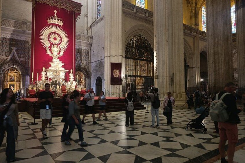 A cathedral interior with a large red altar, a checkered floor, and tall columns. 3