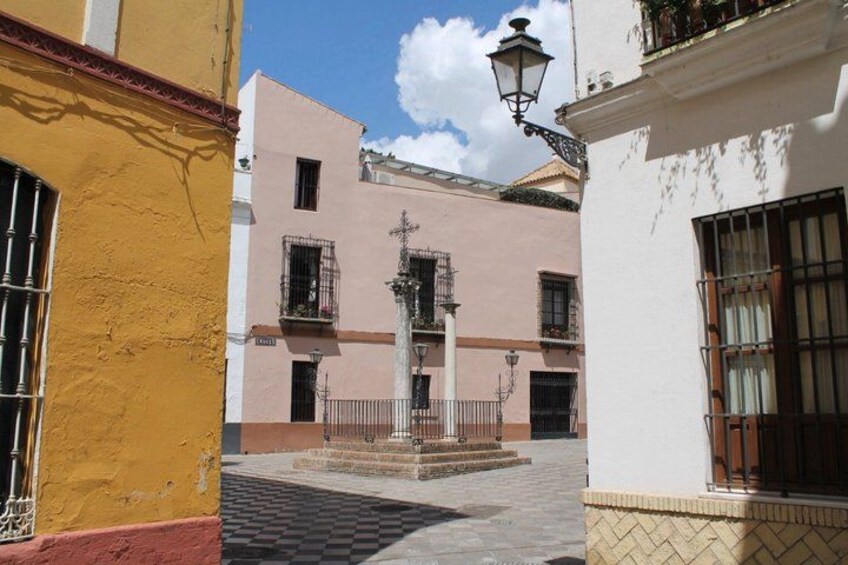 A narrow street with buildings painted in yellow and pink, a street lamp, and a tiled pavement. 3