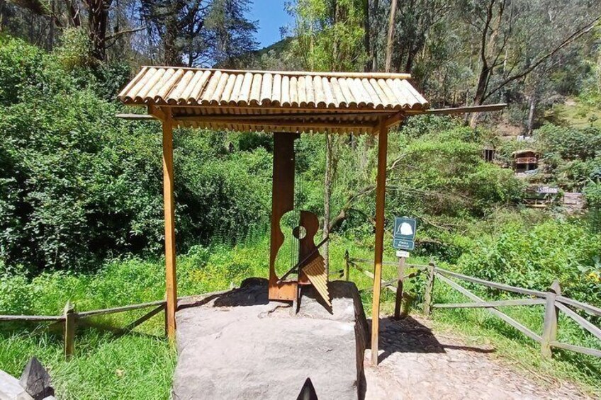 A wooden gazebo with a tiled roof, surrounded by lush greenery and a dirt path. 5
