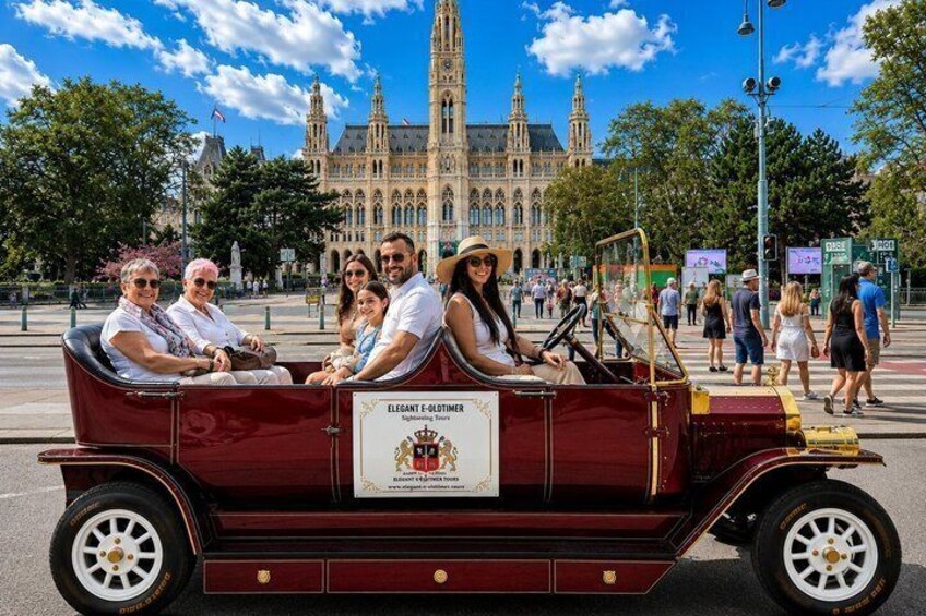 A vintage car with passengers, a historic building in the background, and a clear blue sky. 4