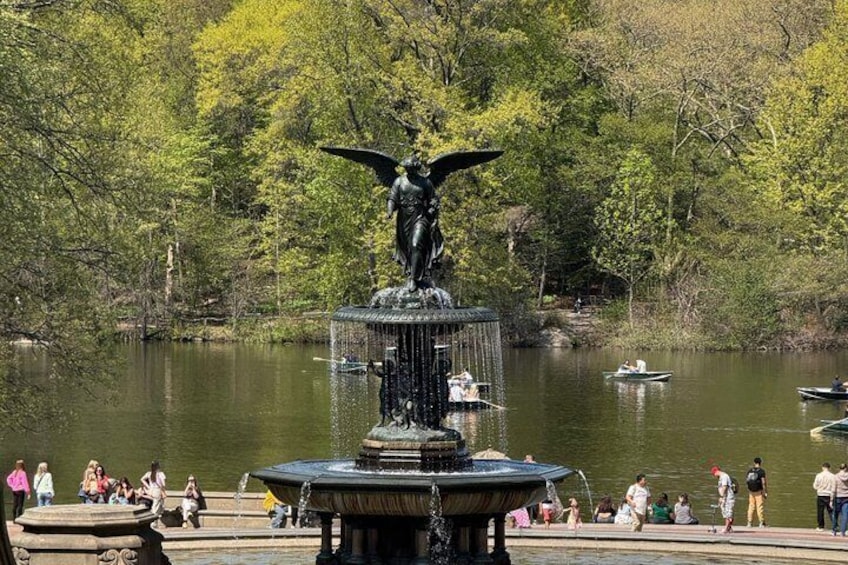 A park with a fountain, people, and boats on the water. 3