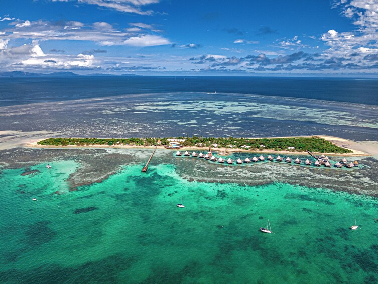 Vue aérienne d’une île tropicale aux eaux turquoise et limpides, avec un long quai et des bungalows sur pilotis. 1