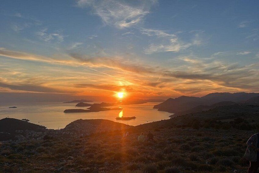 A sunset over a coastal landscape with hills and a body of water. 1