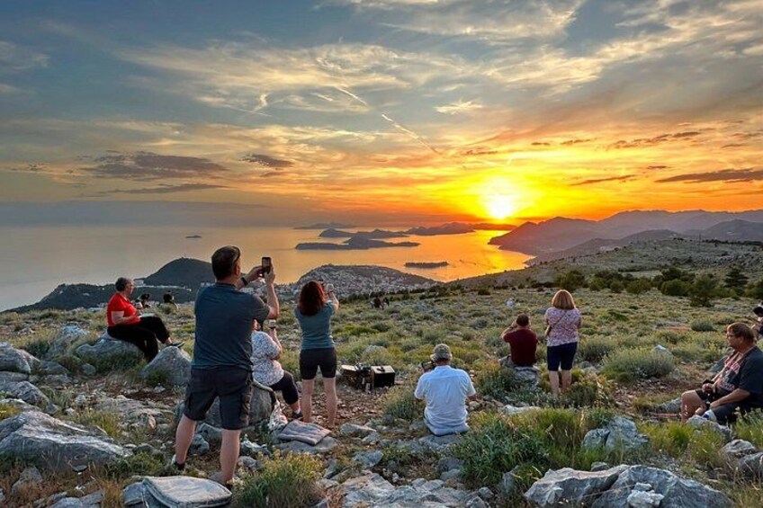 A group of people observing a sunset over a body of water with mountains in the background. 5