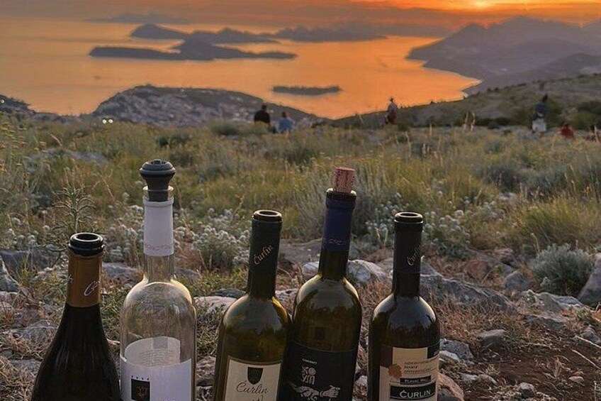 Four wine bottles on a rocky surface with a sunset and mountains in the background. 2
