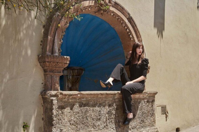A person sitting on a stone ledge next to a blue door with an ornate archway. 3