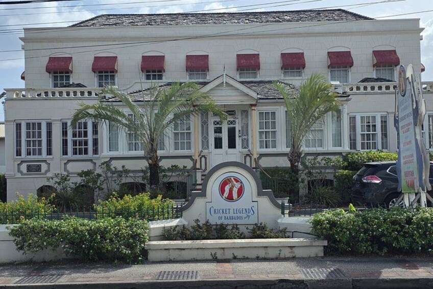 A building with a sign reading 'Cricket Legends' and palm trees in front. 2