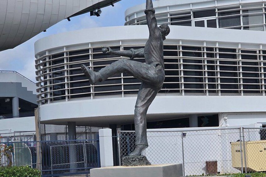 A sculpture of a man in a dynamic pose, a modern building with a grid-like facade, and a chain-link fence in the foreground. 3