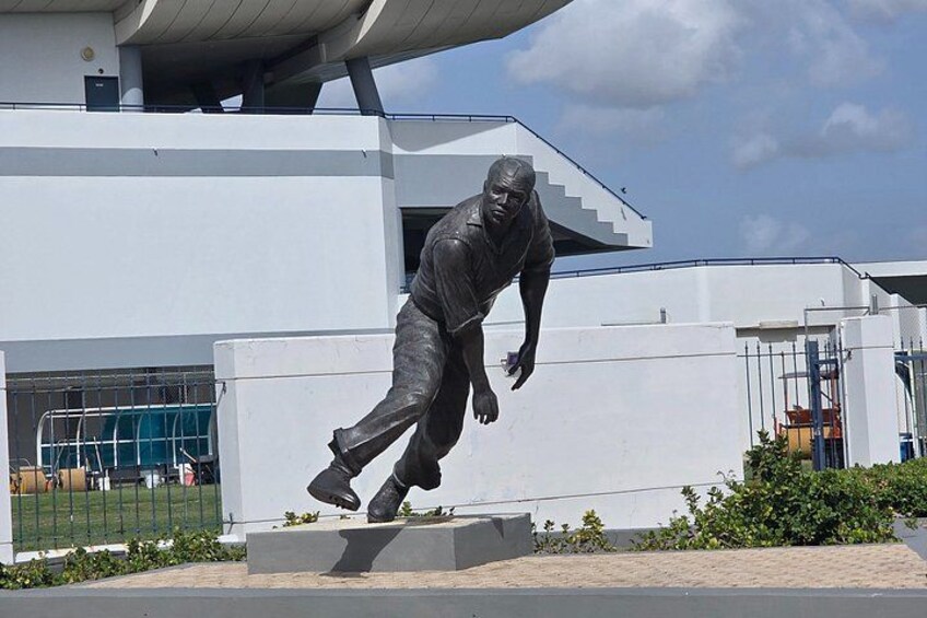 A statue of a man in a dynamic pose, a modern building, and a clear sky. 4