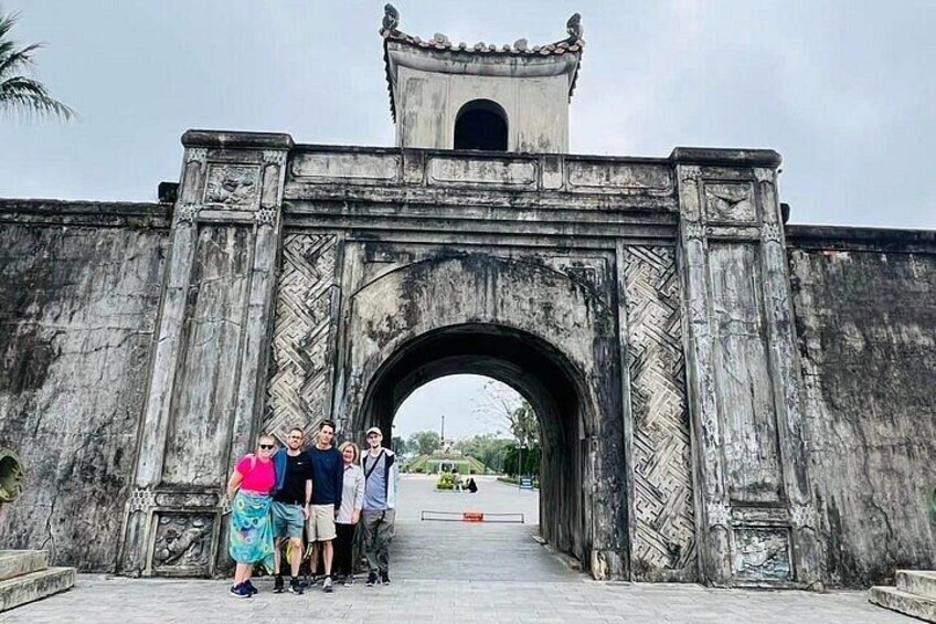 A group of people standing in front of a large stone archway with intricate carvings. 2