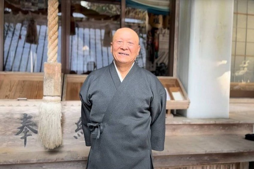 A person in traditional attire standing in front of a building with a wooden structure and a rope. 5