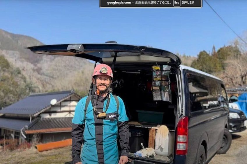 A person standing next to a vehicle with an open back, a mountainous landscape in the background, and solar panels on a building. 3
