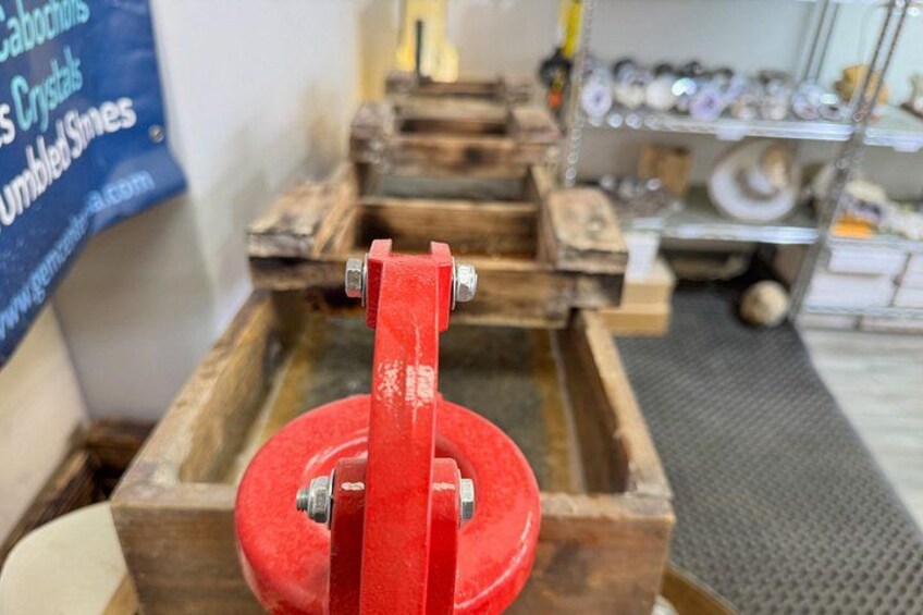 A red mechanical device with a wooden base, possibly a distillation apparatus, in a workshop setting. 5