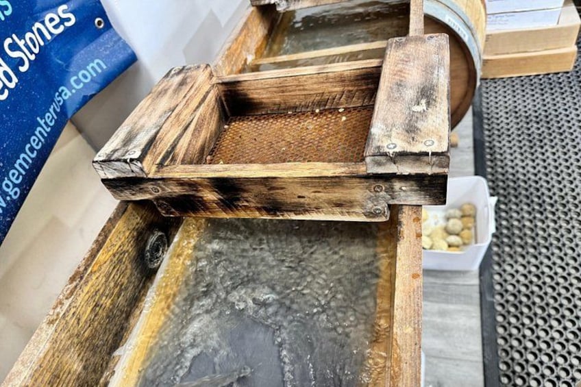 A wooden sieve with a metal mesh, placed on a metal surface, likely for sorting or filtering materials. 3