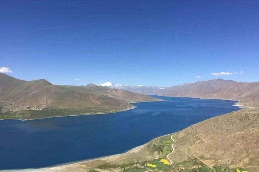 A large lake surrounded by mountains, a winding road, and a clear blue sky. 5
