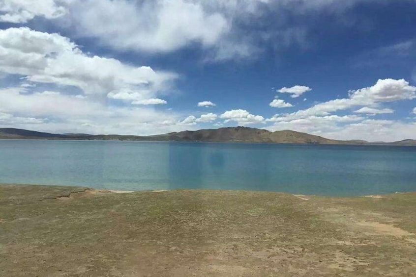 A lake with clear blue water, a grassy foreground, and distant mountains under a partly cloudy sky. 3