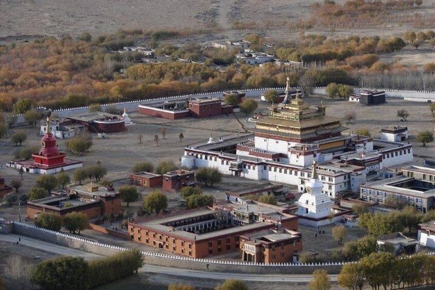 A large, multi-tiered temple complex with a prominent red stupa, surrounded by smaller buildings and sparse vegetation. 1