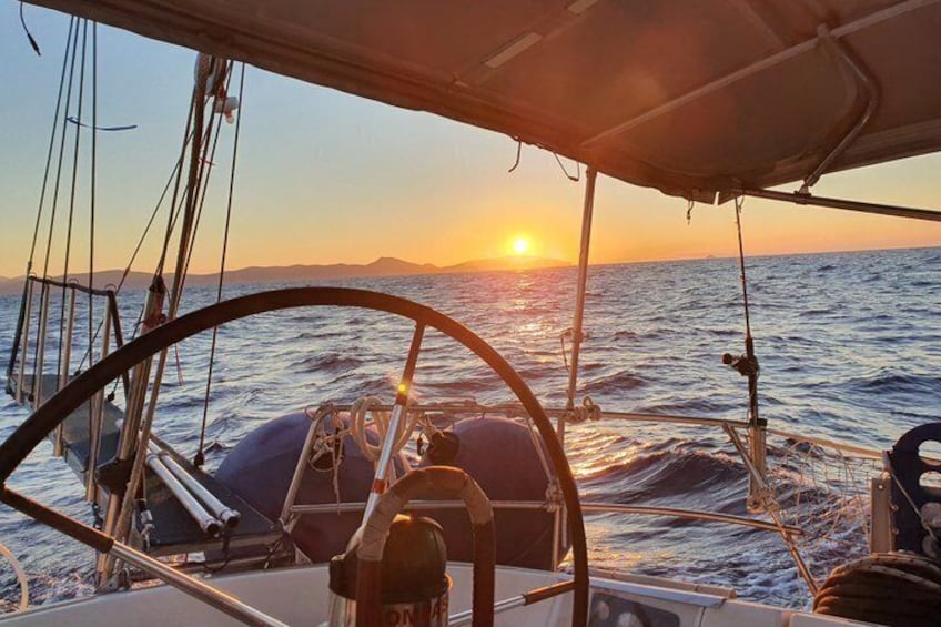 A sailboat at sunset with the sun setting on the horizon. 1