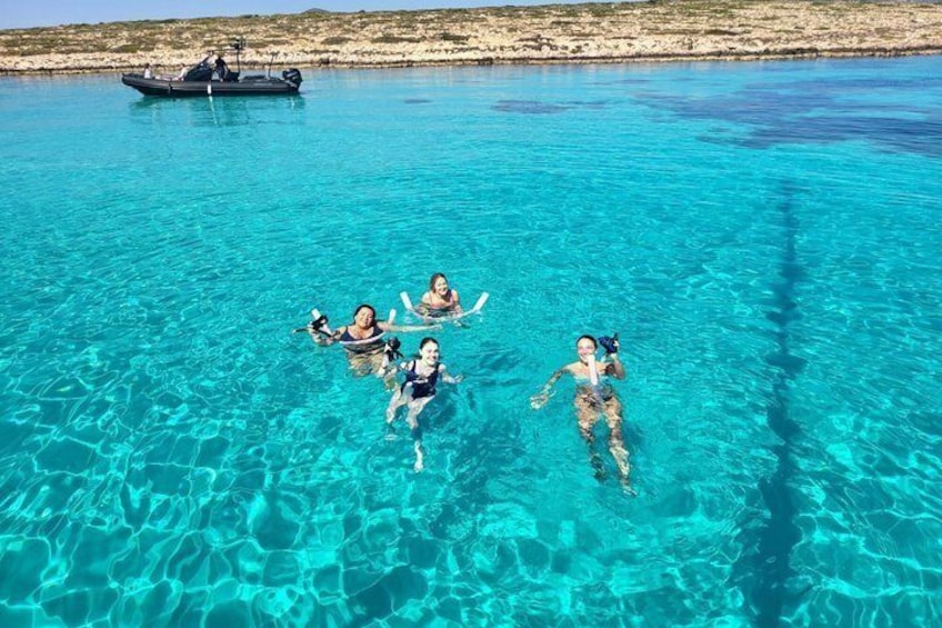 People swimming in clear blue water with a boat in the background. 2