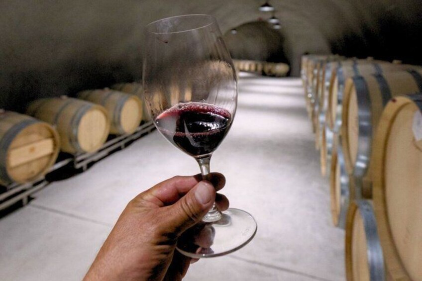 A hand holding a wine glass with red wine, in a cellar with wooden barrels. 5