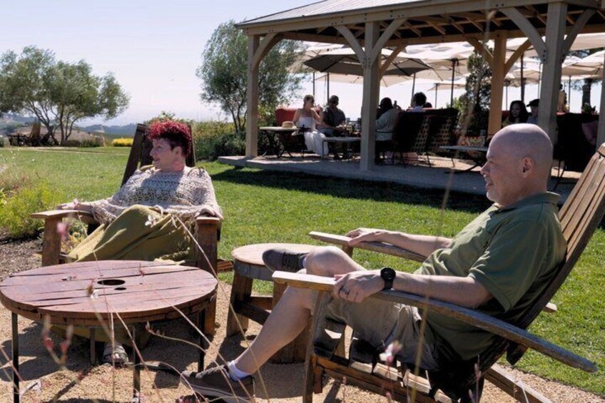 Two people seated at a round table outdoors with a covered seating area in the background. 4