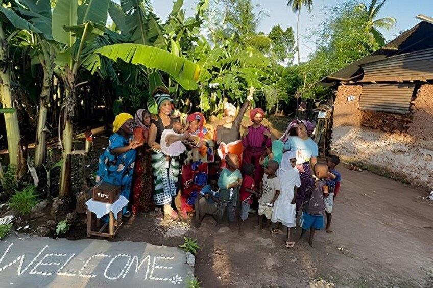 A group of people standing in a rural setting with a welcome sign on the ground. 3