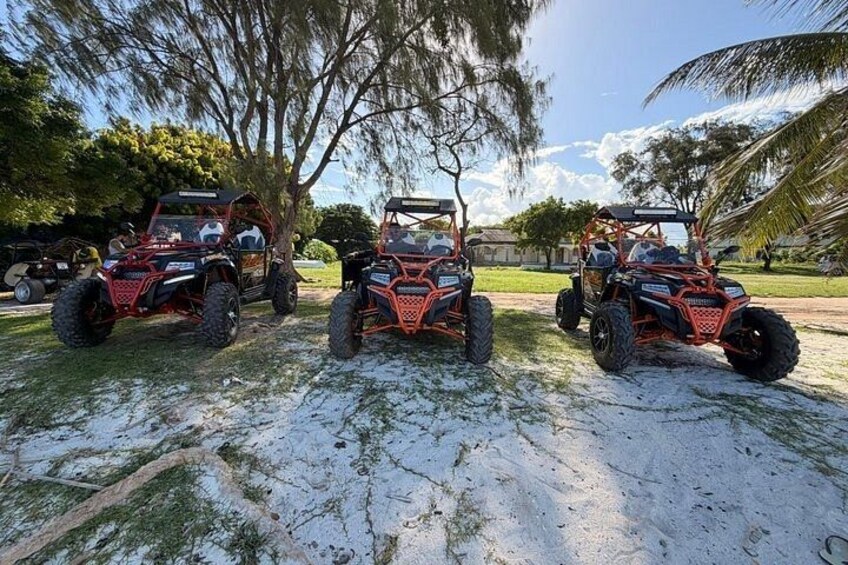 Three off-road vehicles parked on a sandy surface with trees and a clear sky in the background. 5