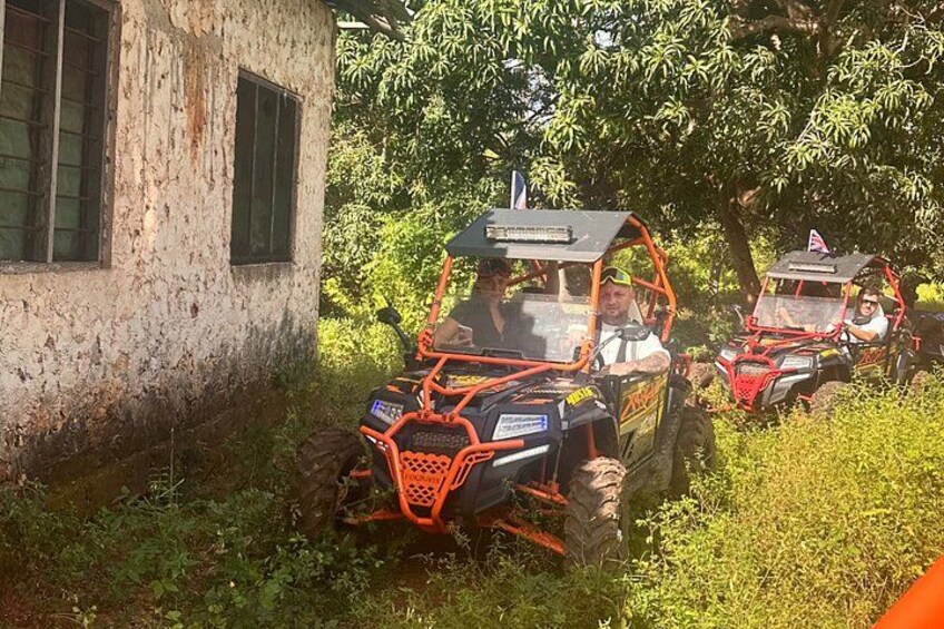 Two off-road vehicles parked near a rustic building surrounded by greenery. 2