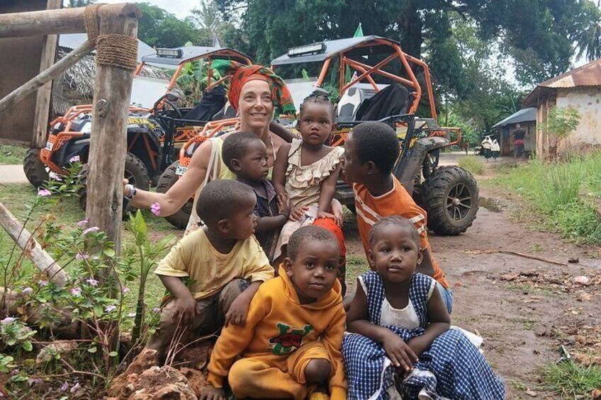 A group of children and an adult in a rural setting with a vehicle in the background. 3
