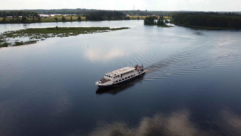 A white riverboat moving across a calm river with surrounding greenery and distant buildings. 5