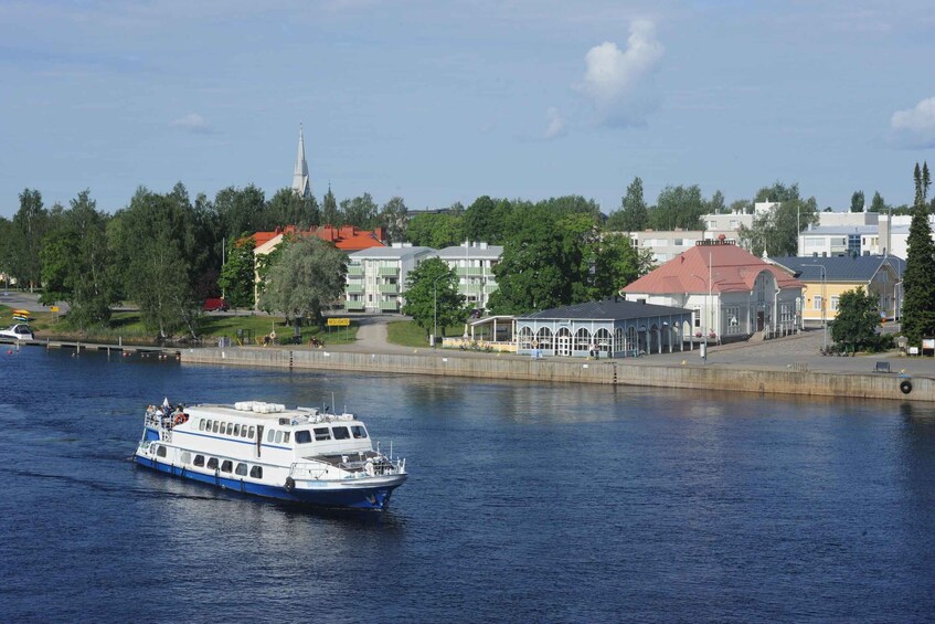 A river with a white and blue boat, buildings, and a church spire in the background. 1