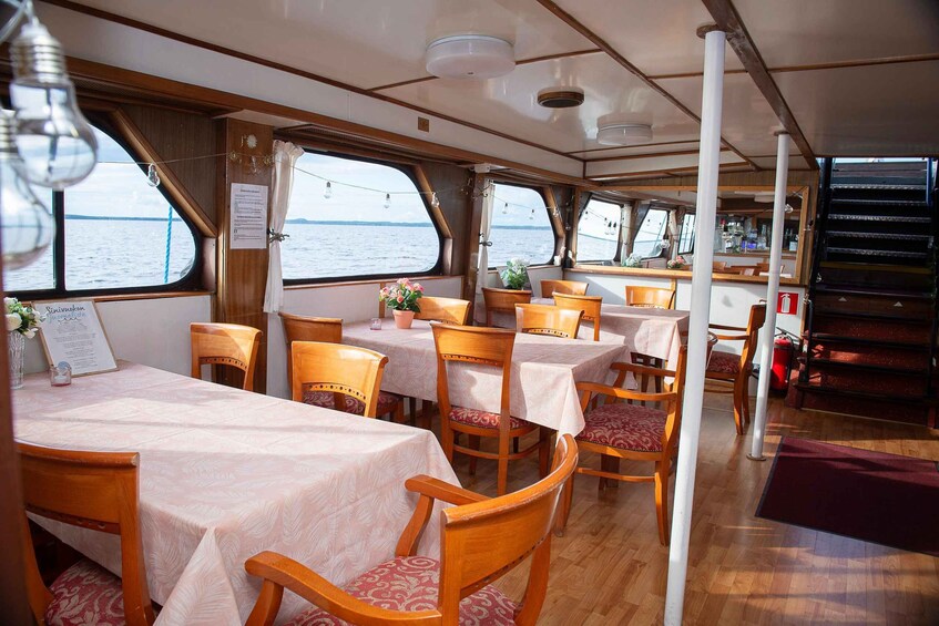 A dining area on a boat with tables and chairs, wooden flooring, and large windows overlooking the water. 4