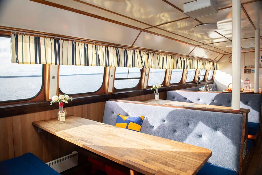 A dining area with wooden tables and cushioned booths, large windows with curtains, and a view of the water outside. 2