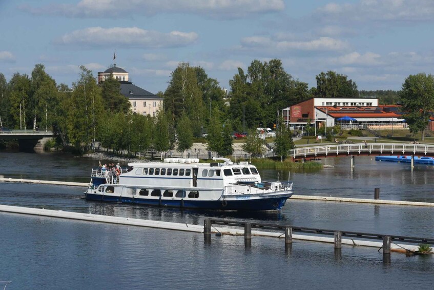A river with a white and blue boat, a bridge, and buildings in the background. 3
