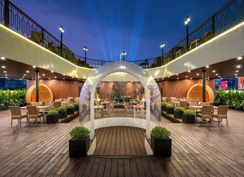 An outdoor dining area with a transparent arch structure, wooden flooring, and surrounding greenery. 5