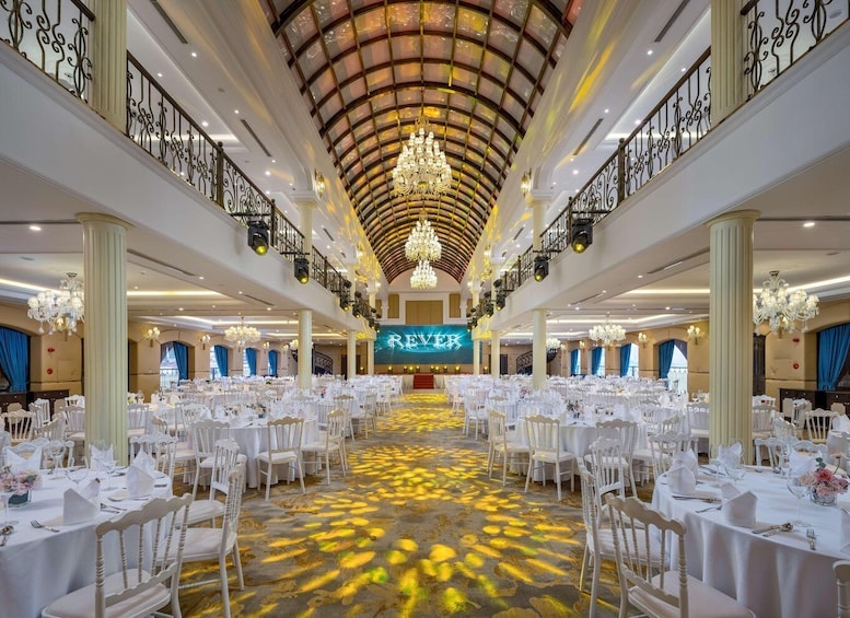 A grand ballroom with white tables, chandeliers, and a large illuminated sign. 3