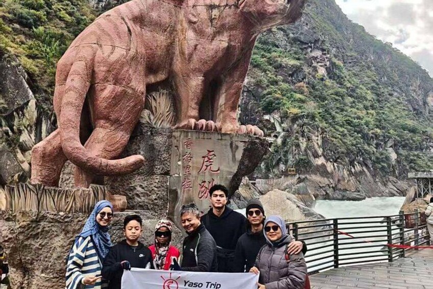 A group of people standing in front of a large animal sculpture, with a river and mountains in the background. 2