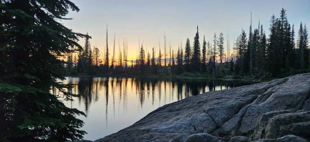 A calm lake surrounded by trees and rocks at sunset. 5