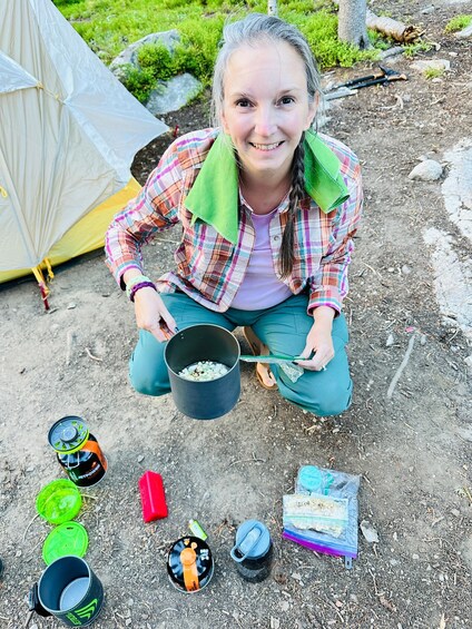 A person cooking outdoors with a pot, surrounded by camping gear and a tent. 3