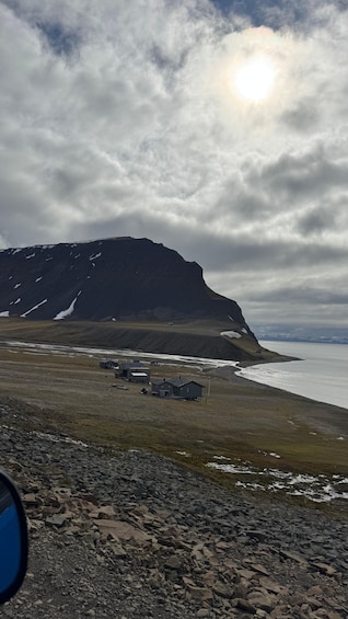 A rugged coastline with a prominent mountain, a small settlement, and a partly cloudy sky. 3