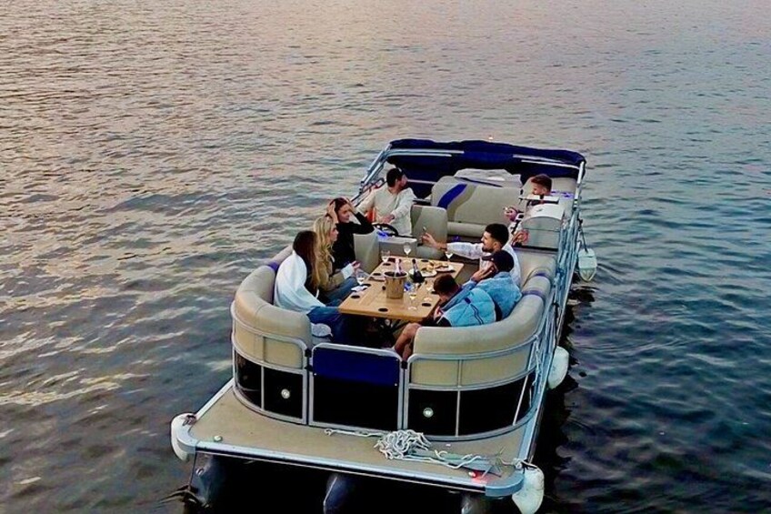 A group of people on a boat with a table and chairs, surrounded by calm water. 5