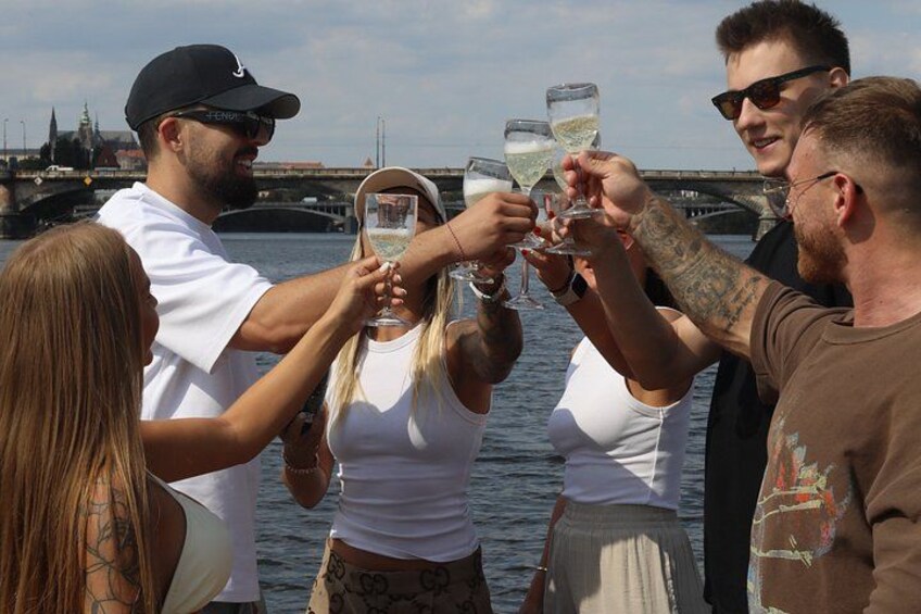 A group of people toasting with champagne glasses by a body of water with a bridge in the background. 2