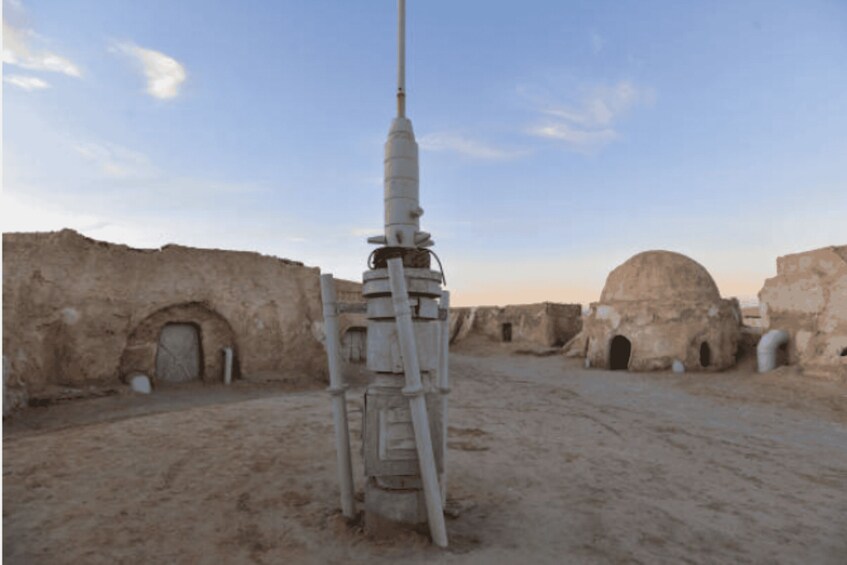 A desert landscape with ancient ruins and a rocket-like structure. 2