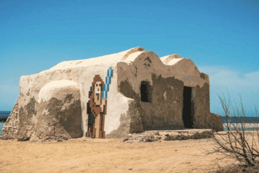 A sandy beach with a small, weathered building featuring a blue door. 5